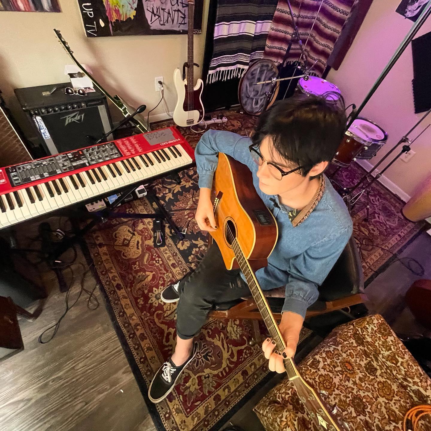 Quinn Decker playing guitar in their home studio surrounded by instruments